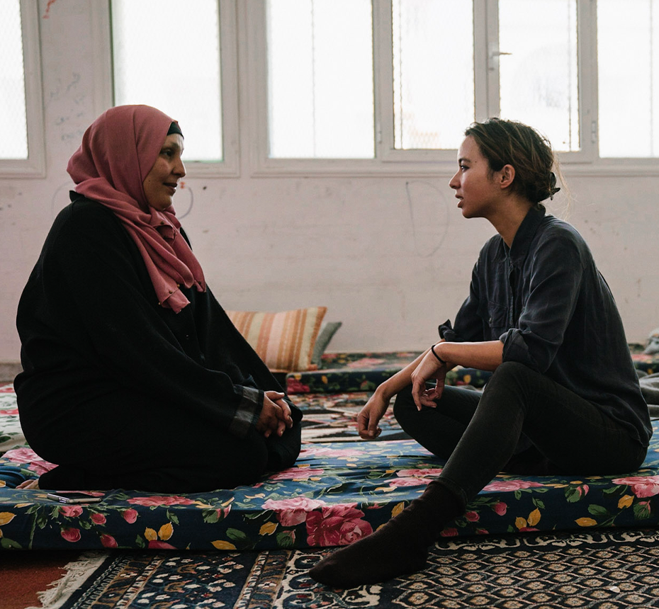 Journalist Isobel Yeung in the field interviewing a woman sitting on a carpeted floor